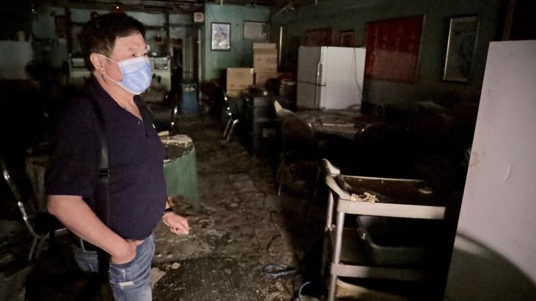 A man in a blue facemask stands among rubble and debris.