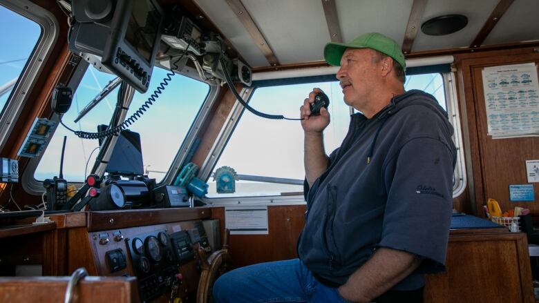 A captain holds a mic up to him at the controls of a boat.