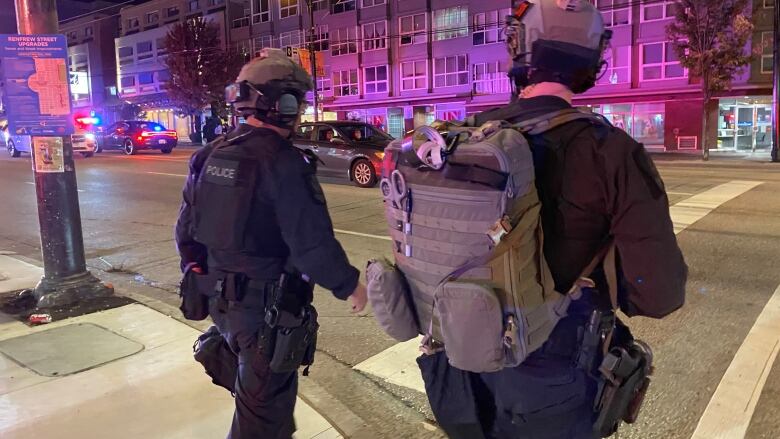 Two police officers wearing tactical gear are shown from behind as they cross a Vancouver street.