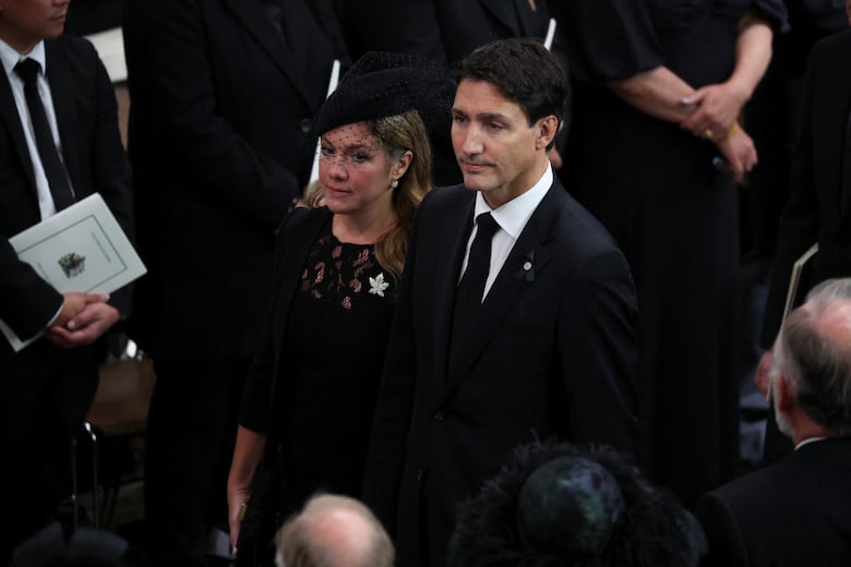 A man and a woman dressed in black formal wear stand amid a crowd.