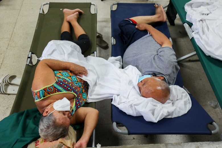 Two people lie on cots in a hurricane shelter.