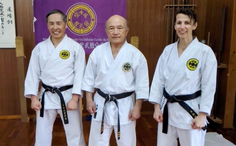 Two men and one woman smile as they pose for a photo wearing their white karate uniforms.