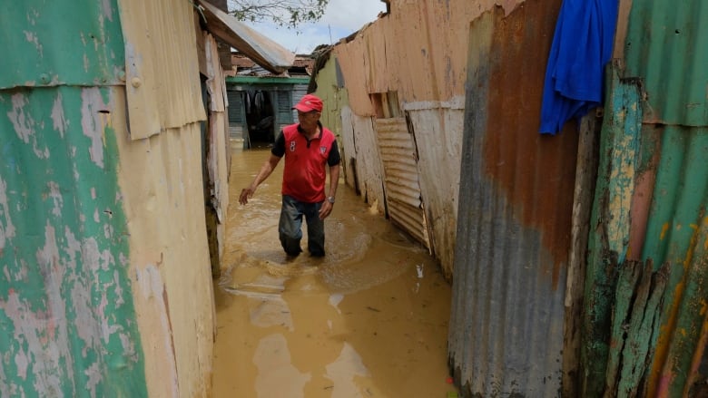 A man wades in floodwater outside a home