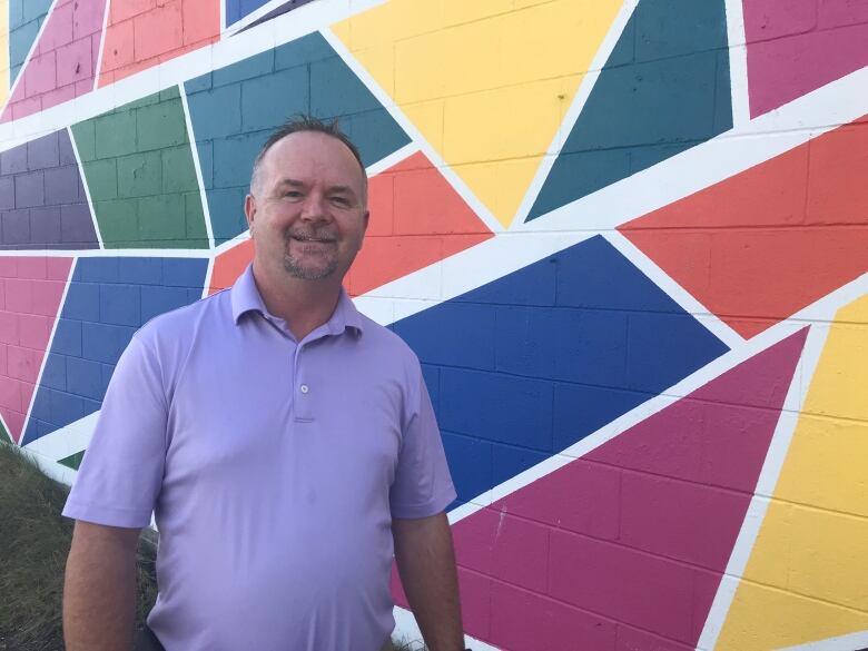 Don Gravelle stands in front of a colourful mural painted on the wall of a coffee shop in downtown Sudbury.