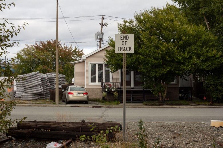 A sign says end of track. Behind it, is a small house.