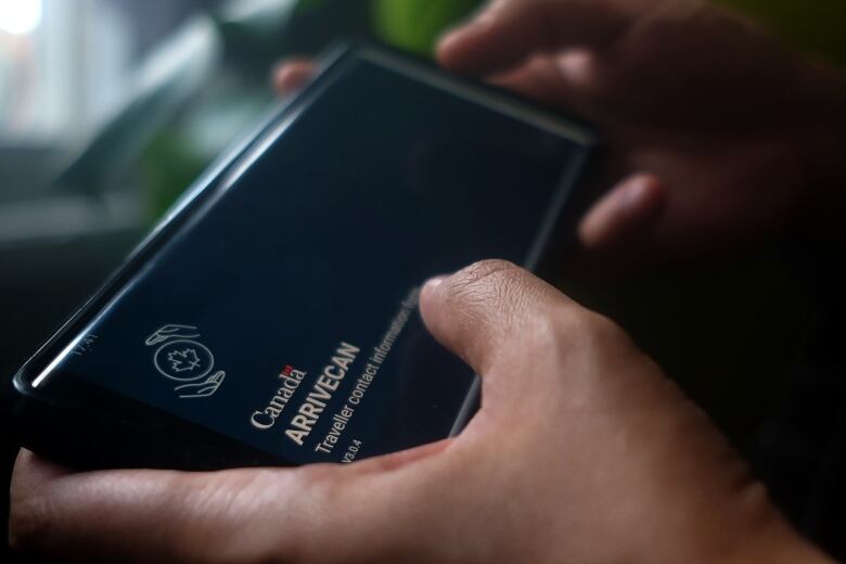 A person holds a smartphone set to the opening screen of the ArriveCan app.