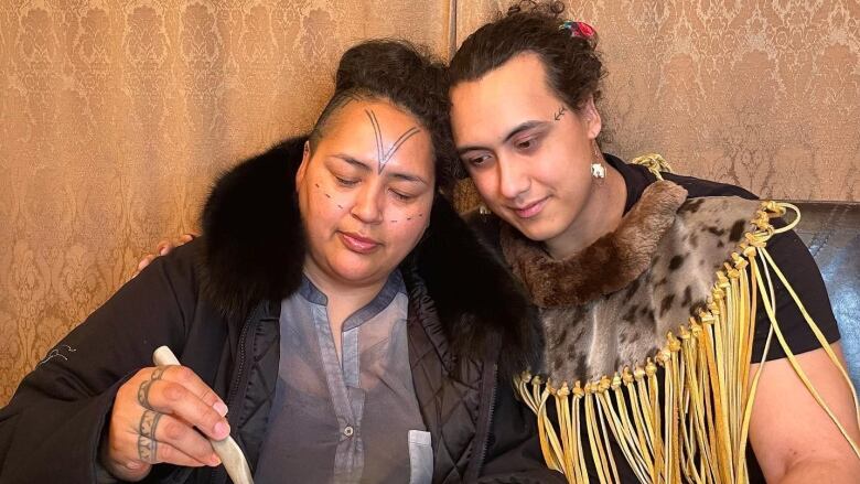 Woman with Inuit forehead tattoos, adult son looking on as she slices blubber.