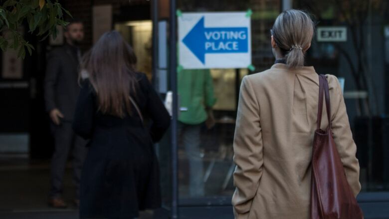 Two women walk into a door with a sign that reads 'VOTING PLACE'.