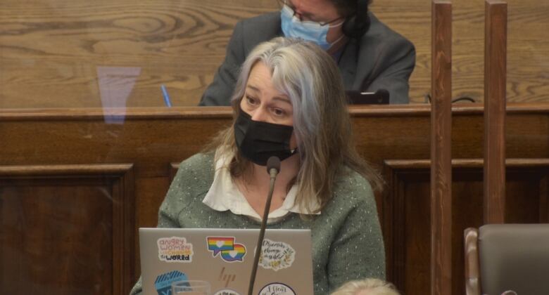 A woman with a mask sits behind a computer laptop in the P.E.I. legislature. 