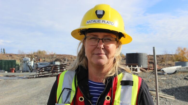 A woman with a safety vest and yellow hard hat. She's outside.