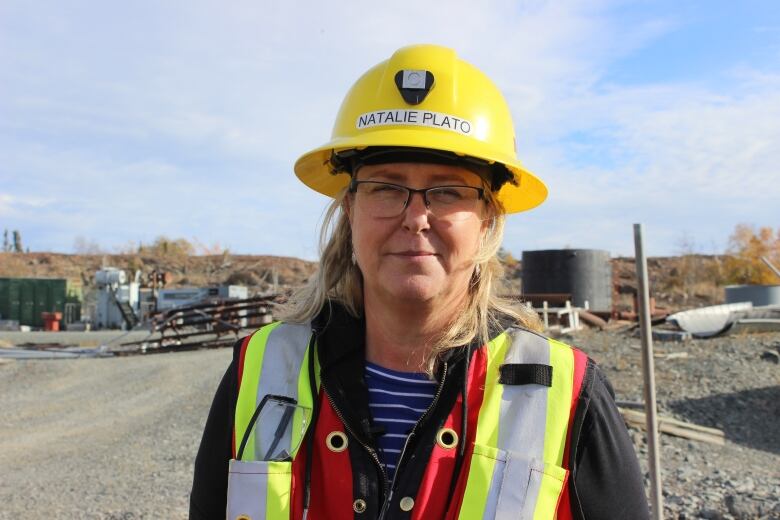 A woman with a safety vest and yellow hard hat. She's outside.