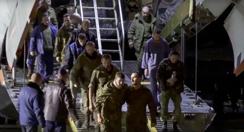 More than a dozen men in dark clothing are seen getting off a plane. 