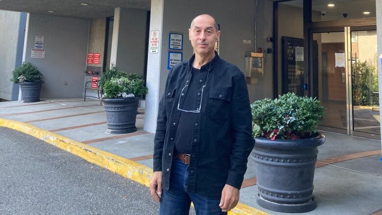 A middle-aged man stands outside a tower apartment.