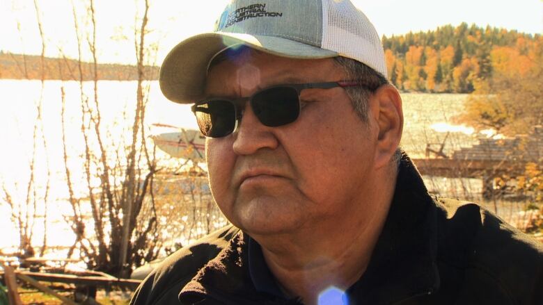 A close-up portrait of a man outside wearing sunglasses and a ball cap.