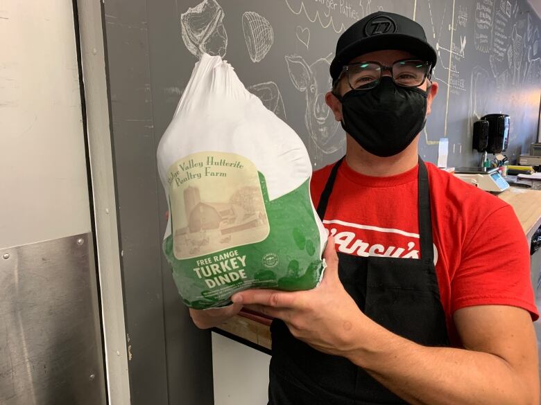 A man in red shirt and apron holds a frozen turkey. 