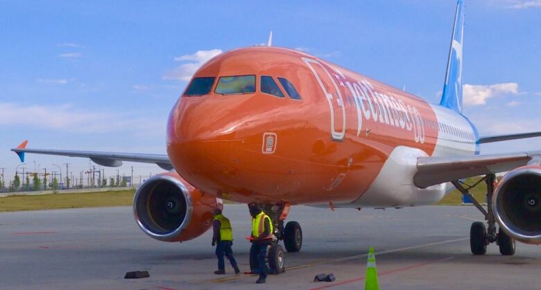 Orange, blue and white Canada Jetlines plane on tarmac, taken from a front angle