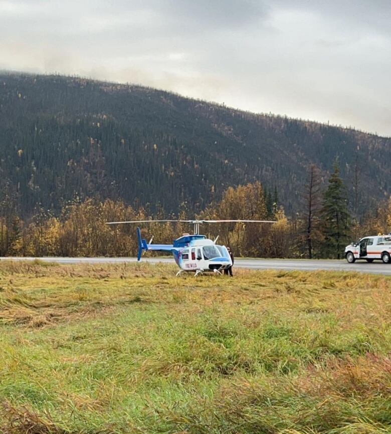 Helicopter sitting on the side of the road in a field.