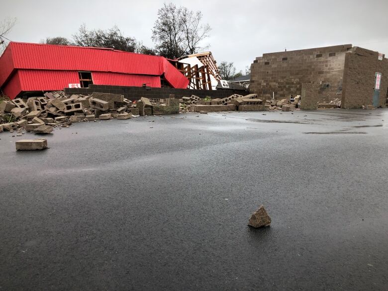 The walls and roof of a car wash are blown off their foundation, leaving behind a pile of rubble.