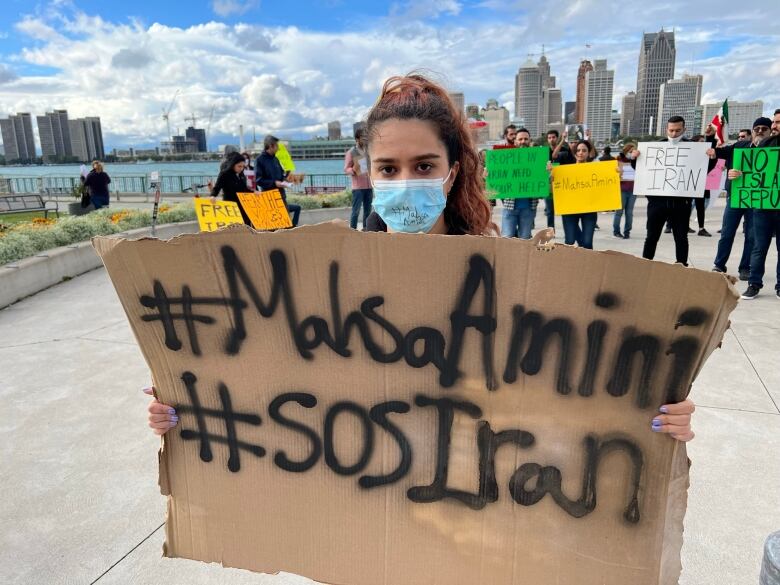 Mahi Sole holding a sign that says hashtag Mahsa Amini and hashtag SOS iran