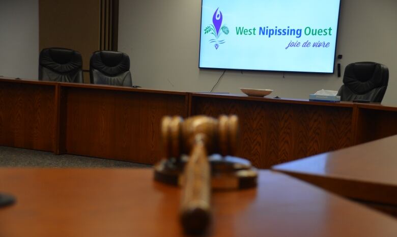 A mayor's gavel sits on a table in an empty council chambers with a West Nipissing logo on a screen on the far wall. 