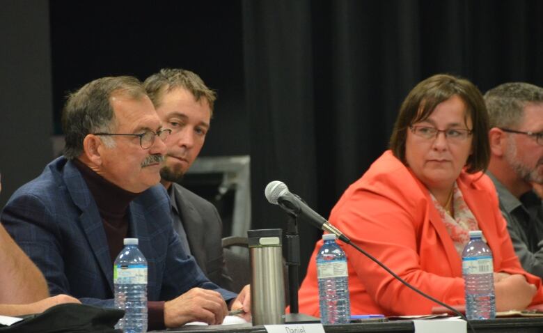 West Nipissing mayoral candidates Dan Roveda, Dave Lewington and Kathleen Thorne Rochon sit at a table on a stage. 