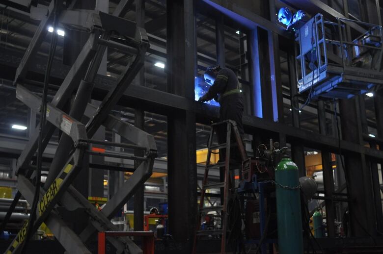 Two people with welding masks on work in dim light with the use of a forklift. 