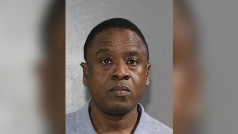 A mugshot of a clean-shaven Black man wearing a grey shirt.