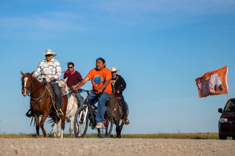 Men ride horses and a bicycle.