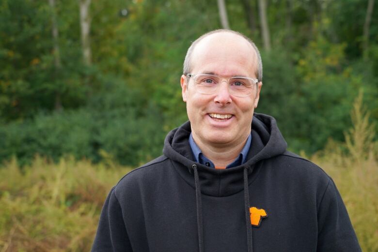 A man wearing glasses and a black hoodie stands in a field.