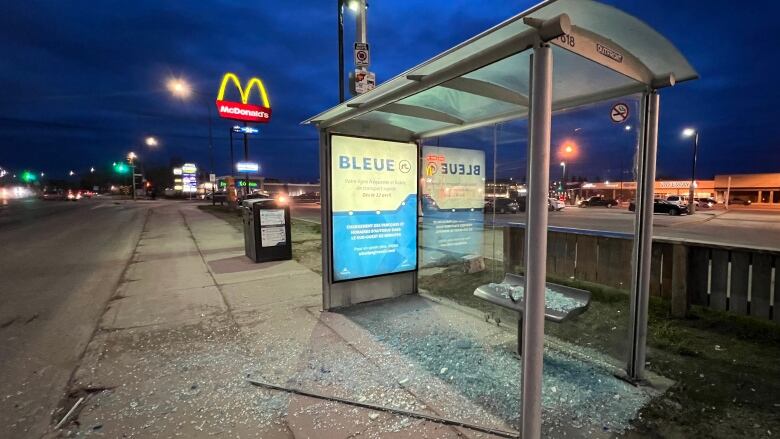 Glass shards spill across the sidewalk from a shattered bus shelter