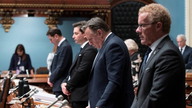 Men in suits look solemn in a legislature.