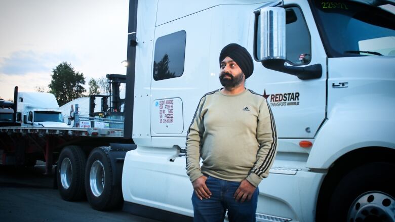 A man stands in front of a semi-trailer cab.