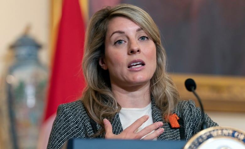 A woman in a grey jacket stands at a podium.