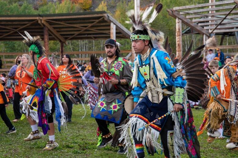 Men gather and dance in their regalia at a powwow.