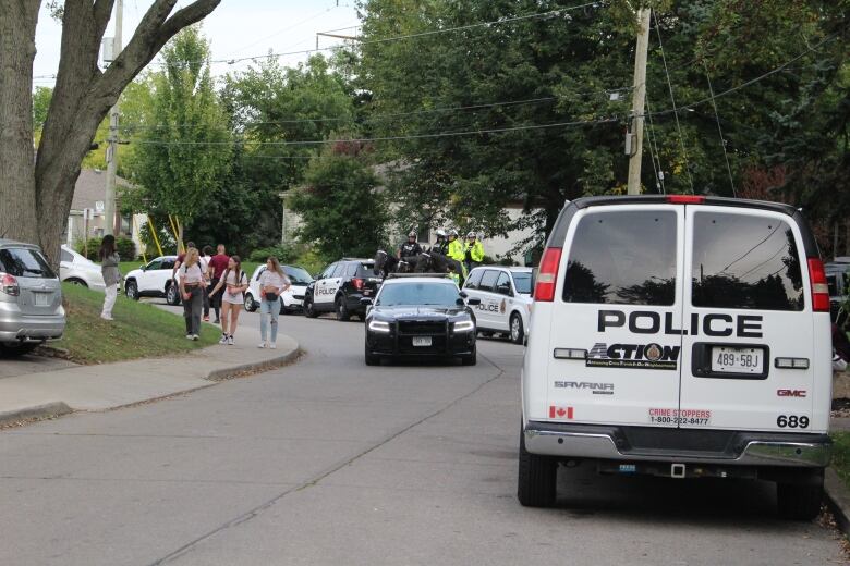 At least 3 police cars parked on a Westdale street and one patrolling the roads as party-goers walk by. 