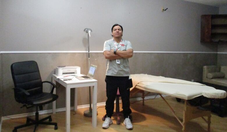 A man stands near a massage bed with his arms crossed.