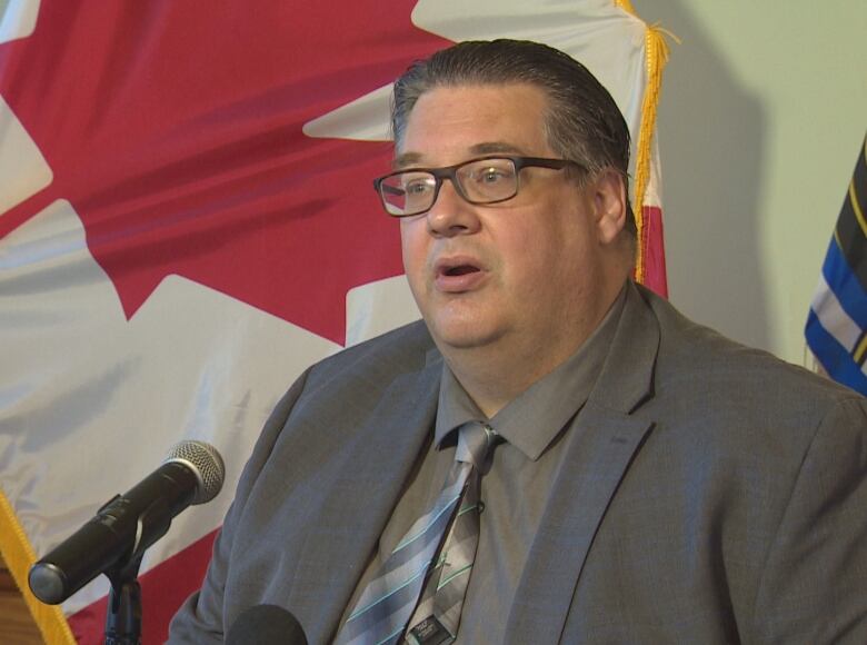 A seated man wearing a suit and tie answers a question before a microphone during a news conference. 