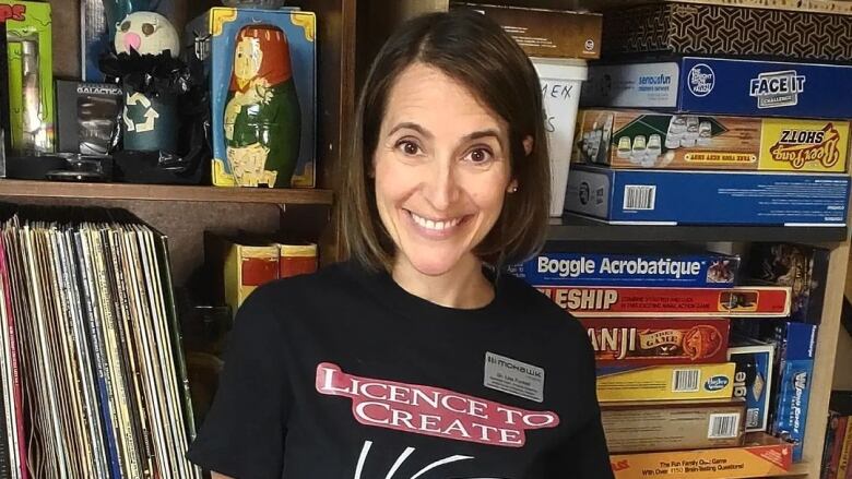 Lisa Funnell stands in front of shelves full of board games, records, and game books, while wearing a shirt 