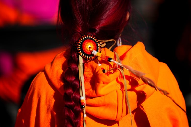 The back of someone's head with a braid and orange beaded medallion. They're wearing an orange hoodie.