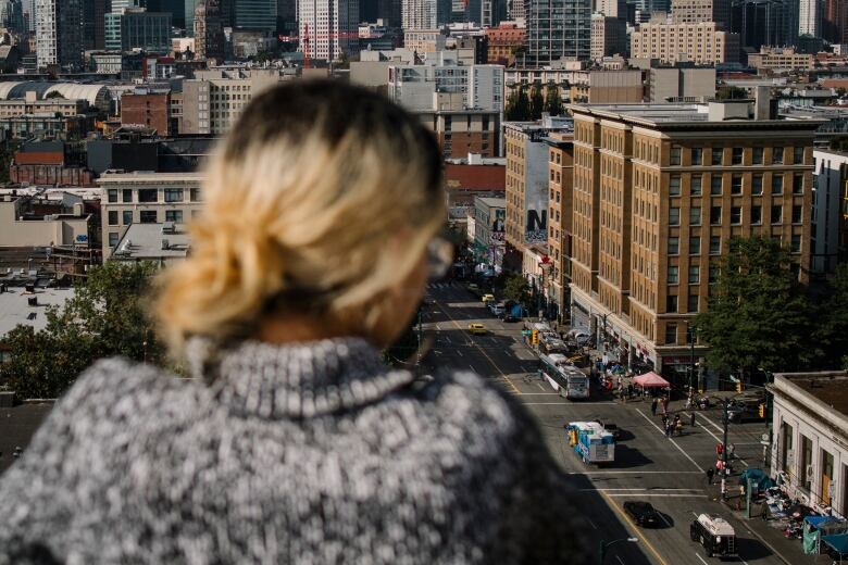 A woman with blonde hair is seen in silhouette, looking over a cityscape.