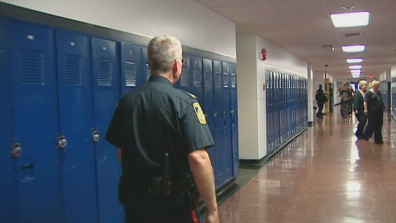 A police officer walks through a school hallway with lockers lining the walls.