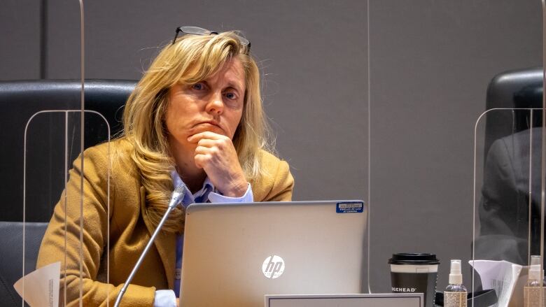 A politician puts her hand on her chin as she listens at her desk.