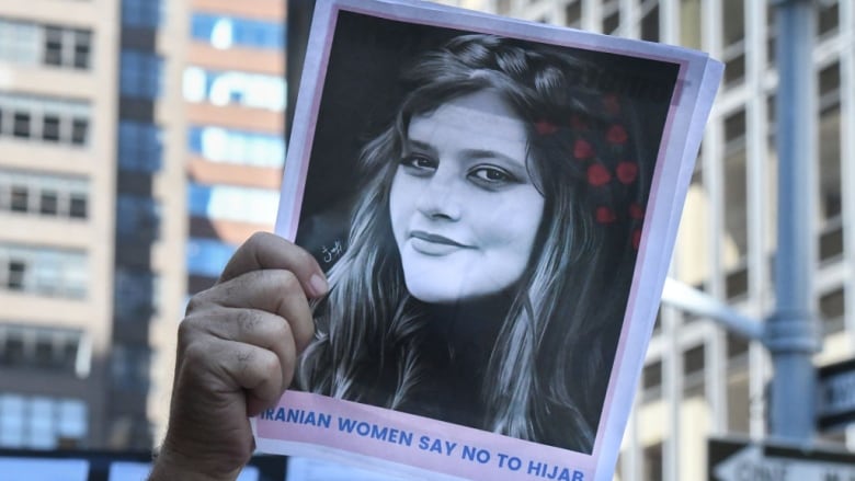 An arm holds up a photo of an Iranian woman in a protest against Iranian President Ebrahim Raisi outside of the United Nations.