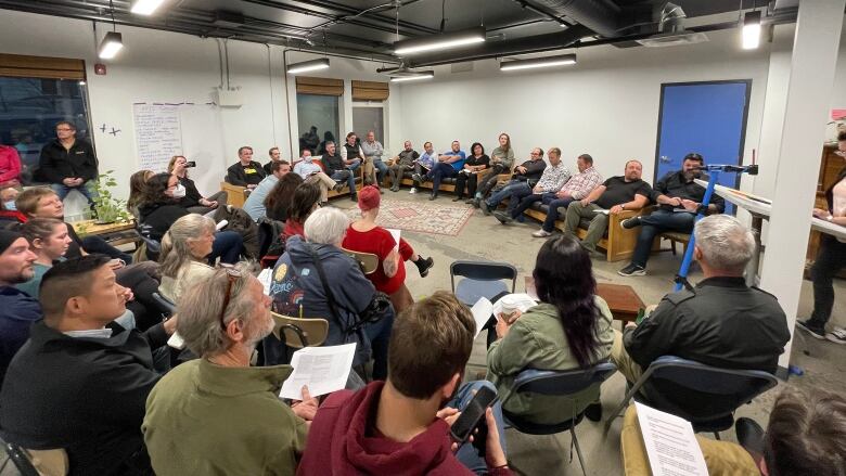 A crowd of people sit in a circle, filling a room.