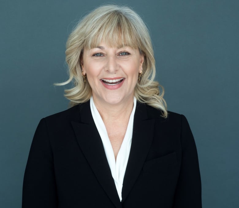 A woman wearing business apparel smiles for a portrait against a blue-green background.