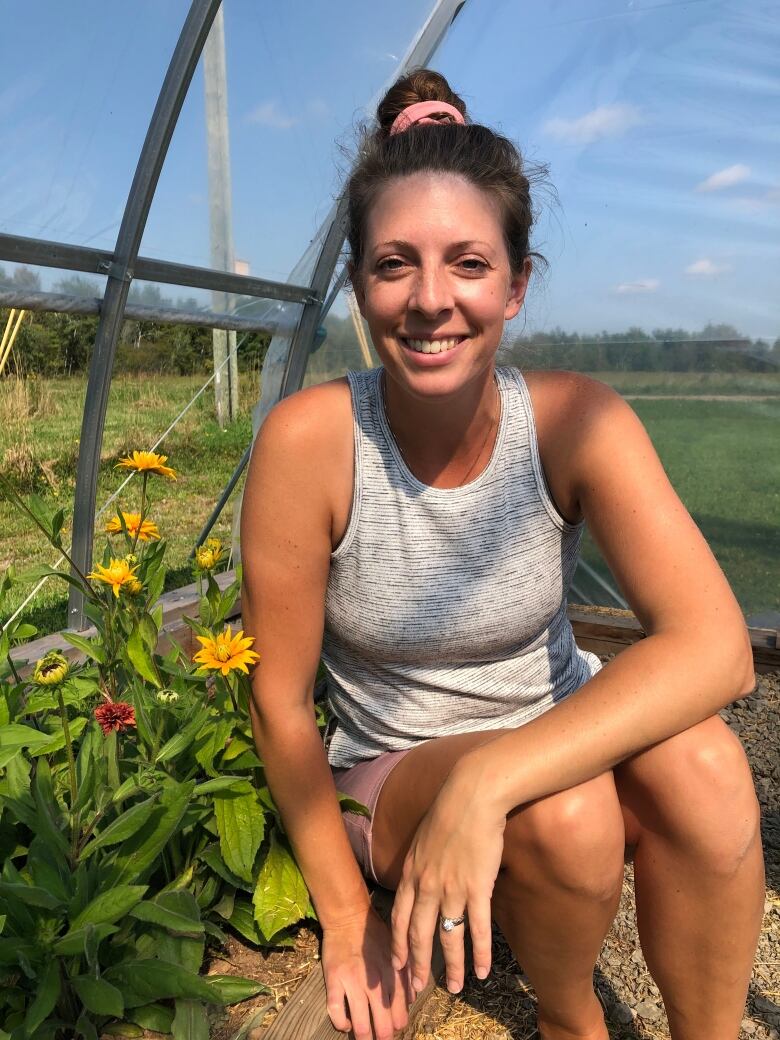 A woman with dark hair crouches beside some yellow flowers in a greenhouse.