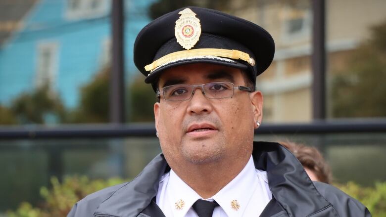 A man in a fire chief's hat stands at a microphone in front of city hall.