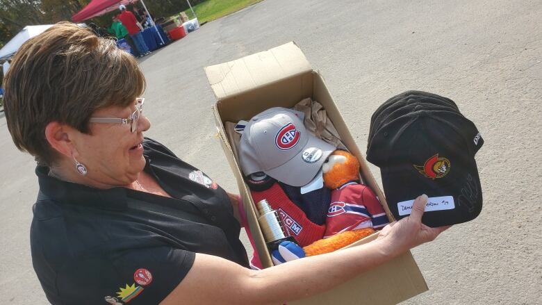 A woman holding a box of hats and other hockey merchandise from the Montreal Canadiens and Ottawa Senators.  