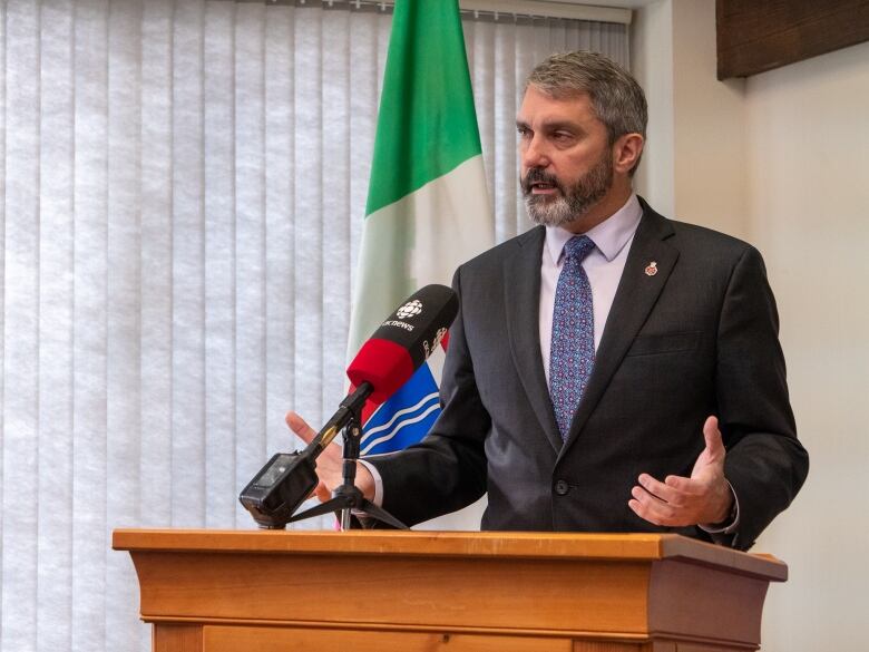 Silver-haired man in suit at podium.