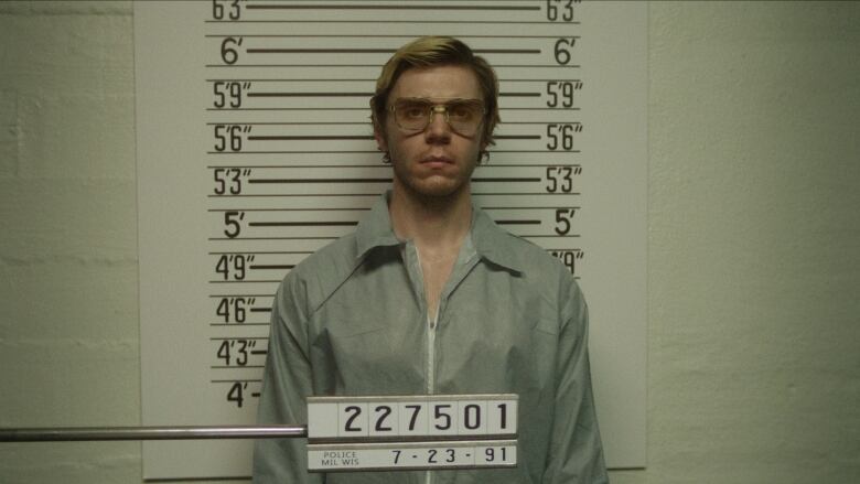 A man in glasses stands in a  police mug shot